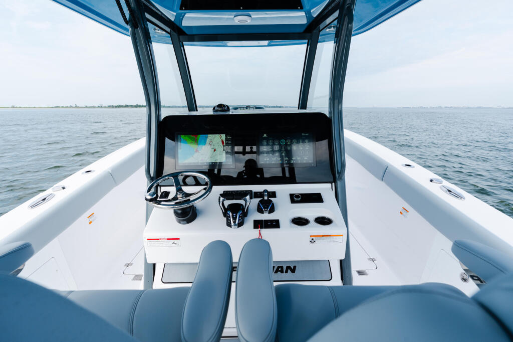 Helm console with touchscreen display, steering wheel, and dual blue seating in a modern center console boat