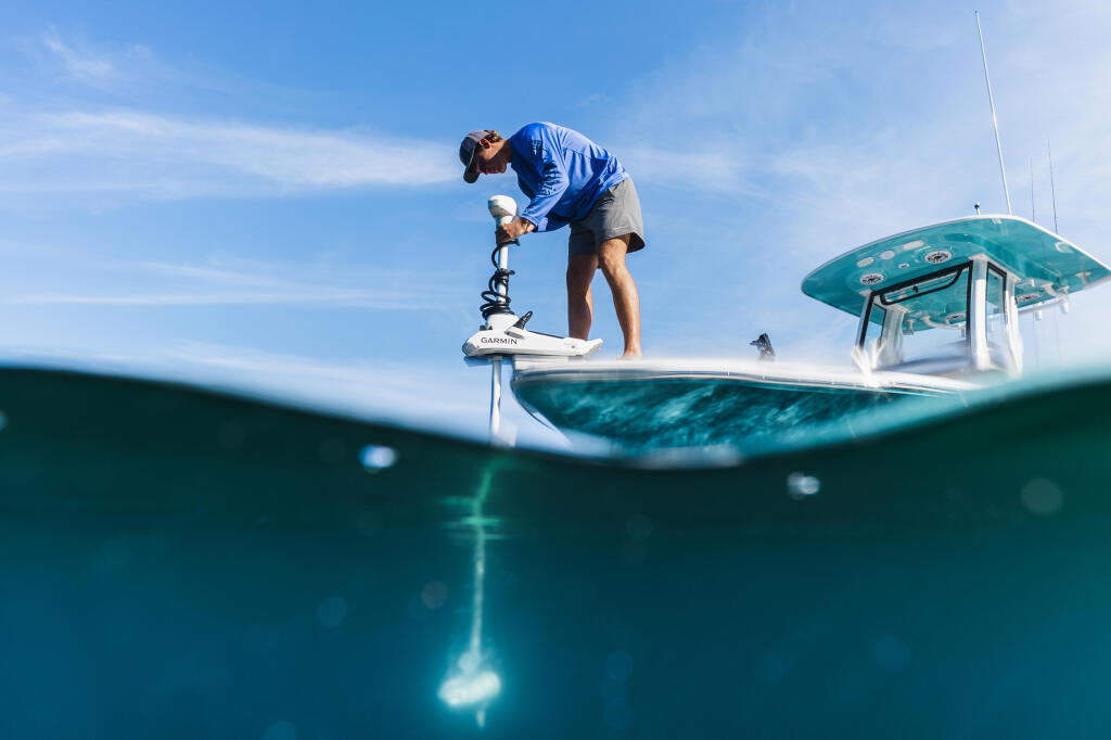Angler operating a Garmin trolling motor on a fishing boat with split underwater and above-water view