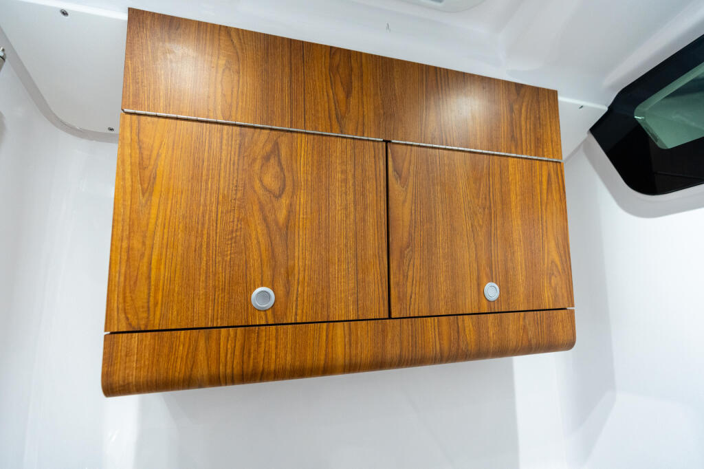 Teak wood storage cabinets with chrome handles mounted on white cabin wall