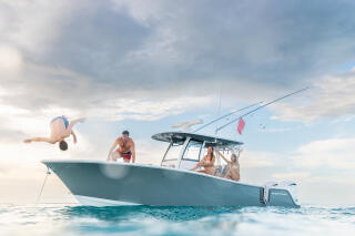 Group of friends enjoying a boat day with one person jumping off the side into clear turquoise water