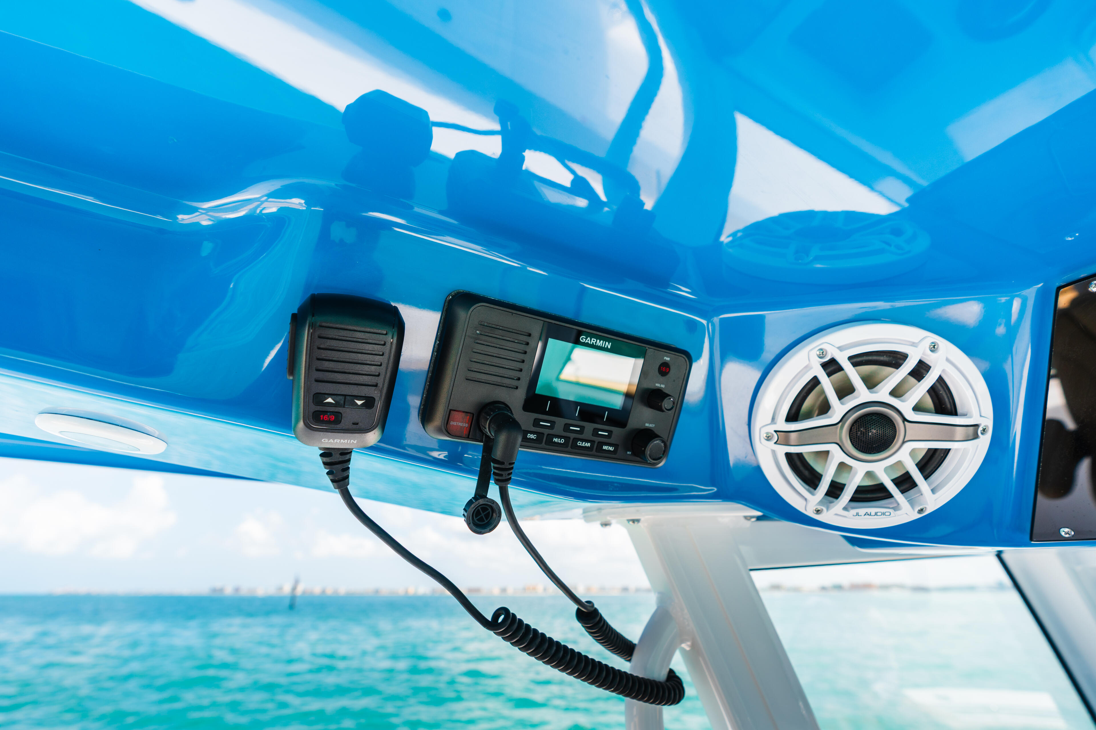 Marine radio, microphone and white speaker mounted on bright blue hardtop with ocean view
