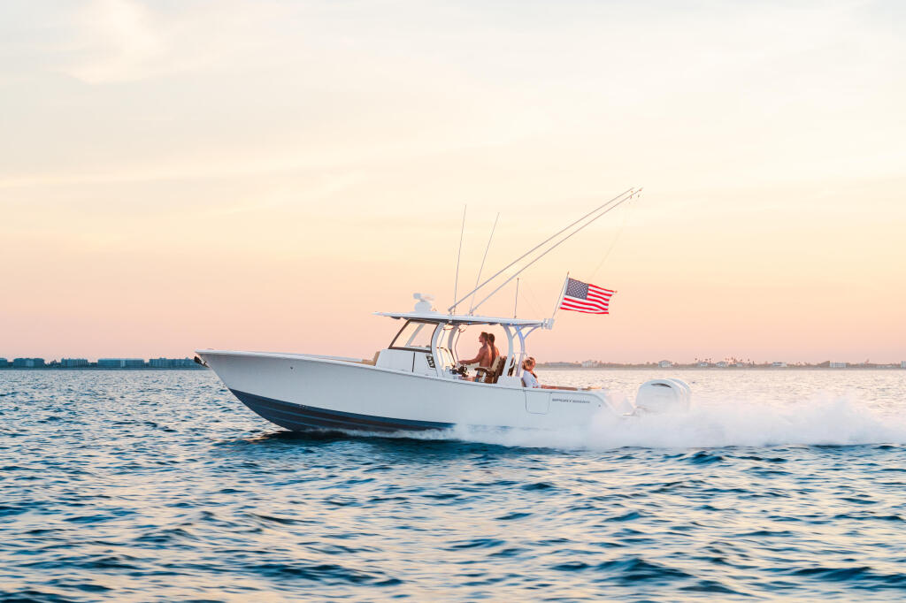 White center console boat running at speed with couple aboard, American flag flying at golden hour