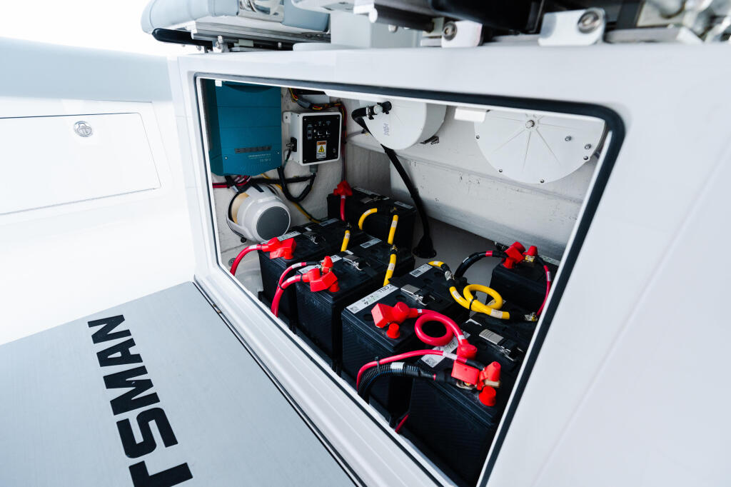 Open storage compartment revealing dual battery banks with red and yellow cables and marine electronics