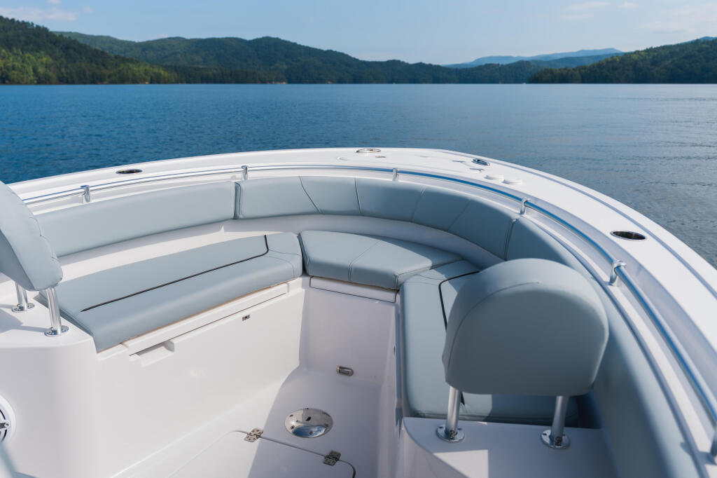 White center console boat with gray upholstered bow seating on calm lake surrounded by forested mountains