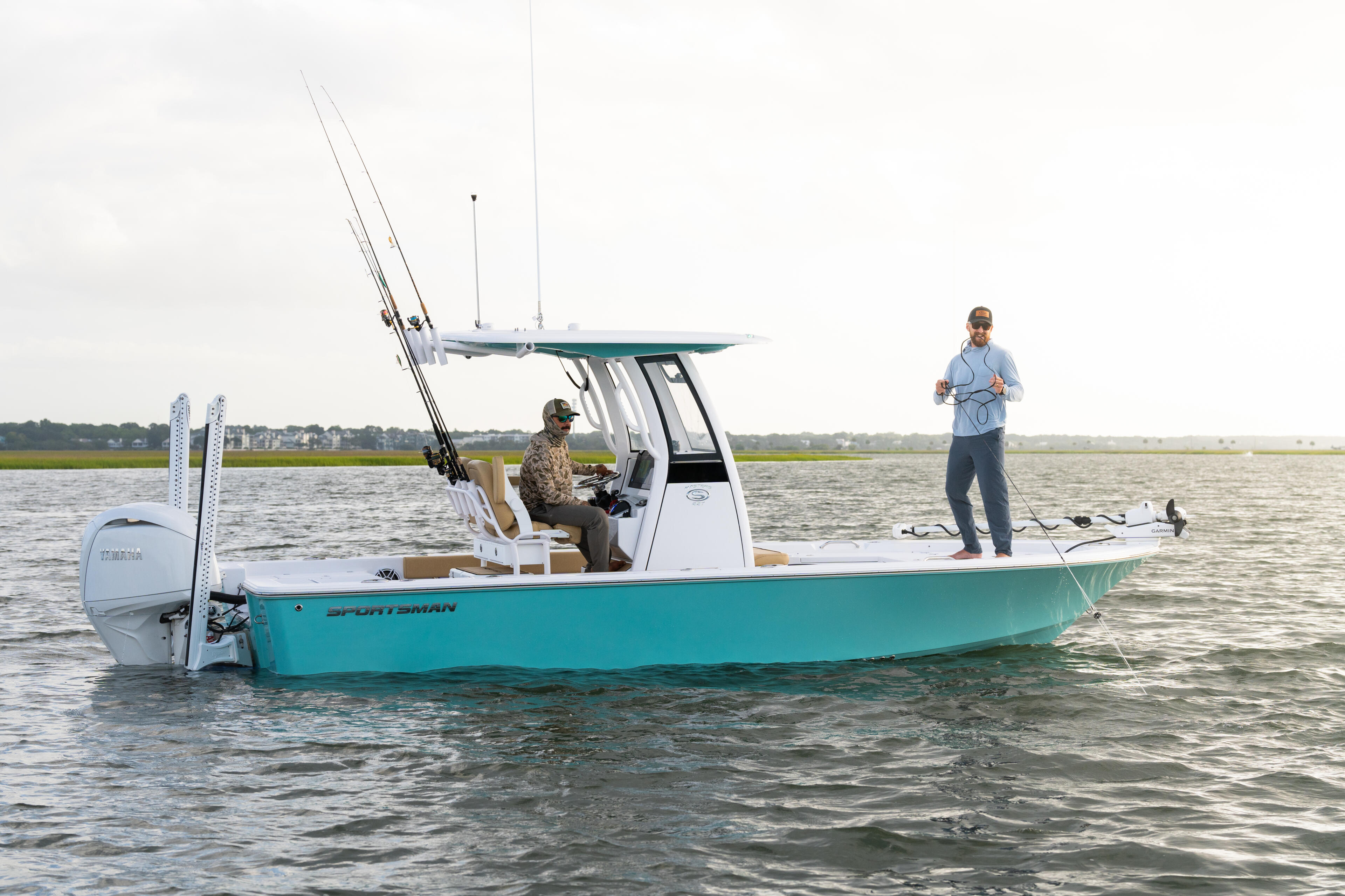 Two anglers on a turquoise Sportsman boat with hard-top fishing in shallow coastal waters
