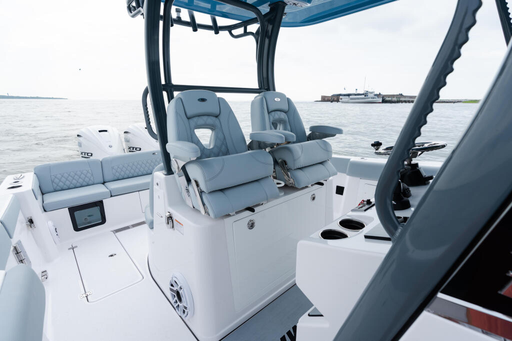 Helm and seating area of a white center console boat with gray upholstered captain's chairs and hard-top frame