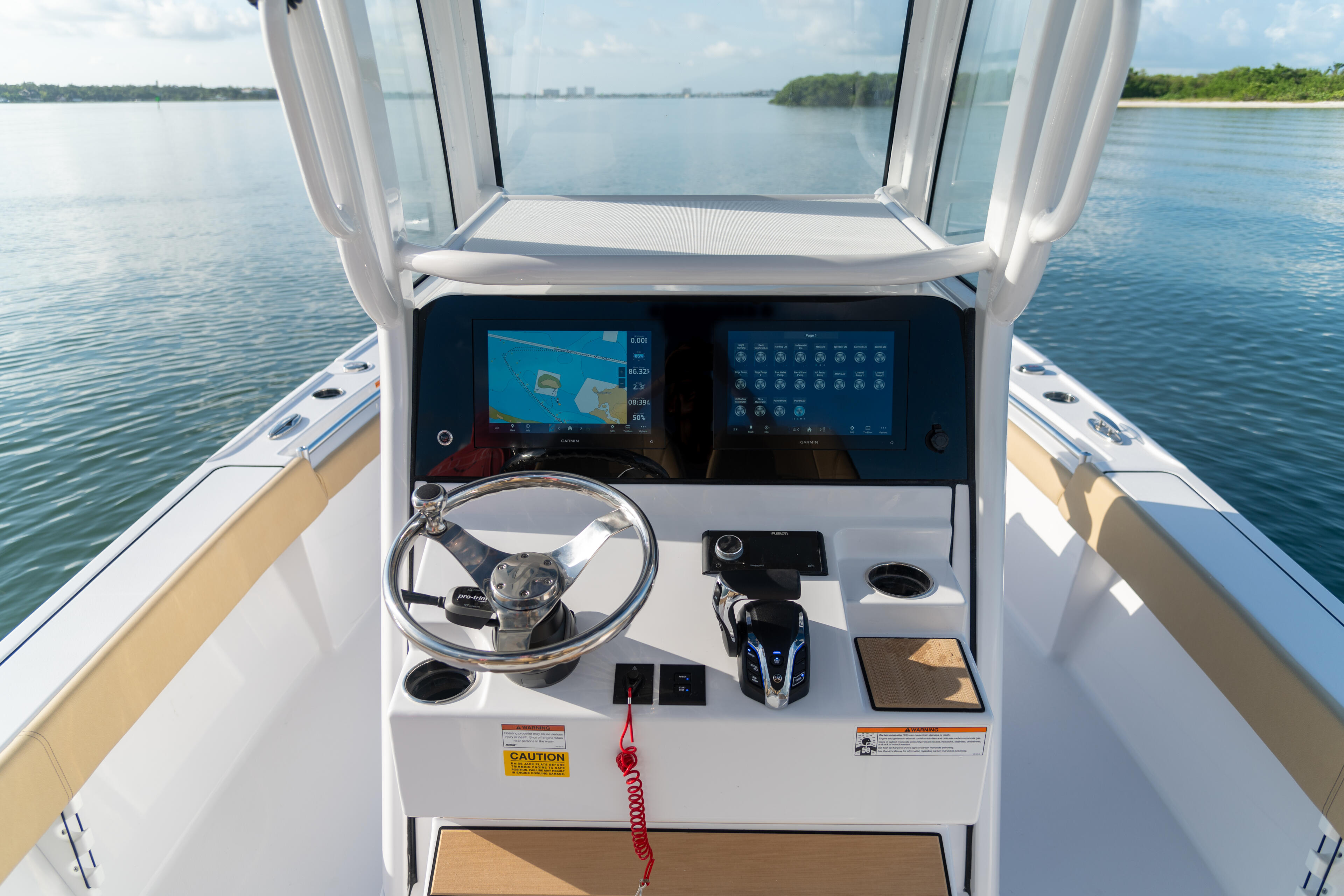 Helm station with dual monitors, steering wheel, and windshield viewing calm blue water and coastline