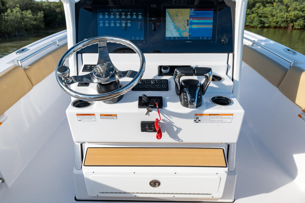 Helm station with dual monitors, stainless steel wheel, and control systems overlooking a waterway