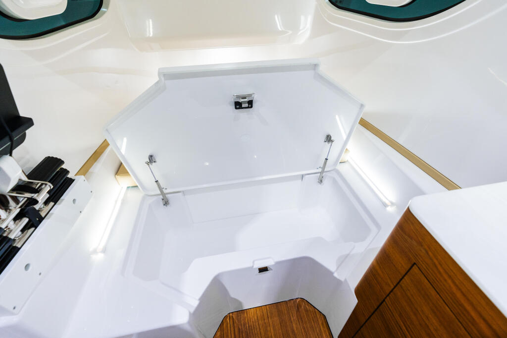 Clean white cabin interior with storage hatch, wood trim, and overhead ventilation windows