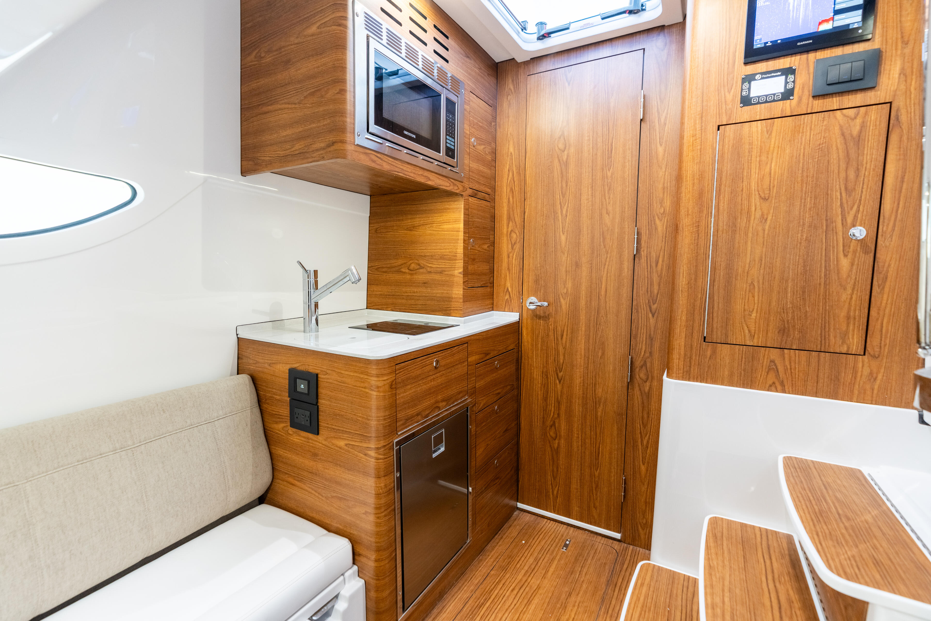 Galley with wooden cabinetry, microwave, sink, and storage in a boat cabin with skylight and electronics display