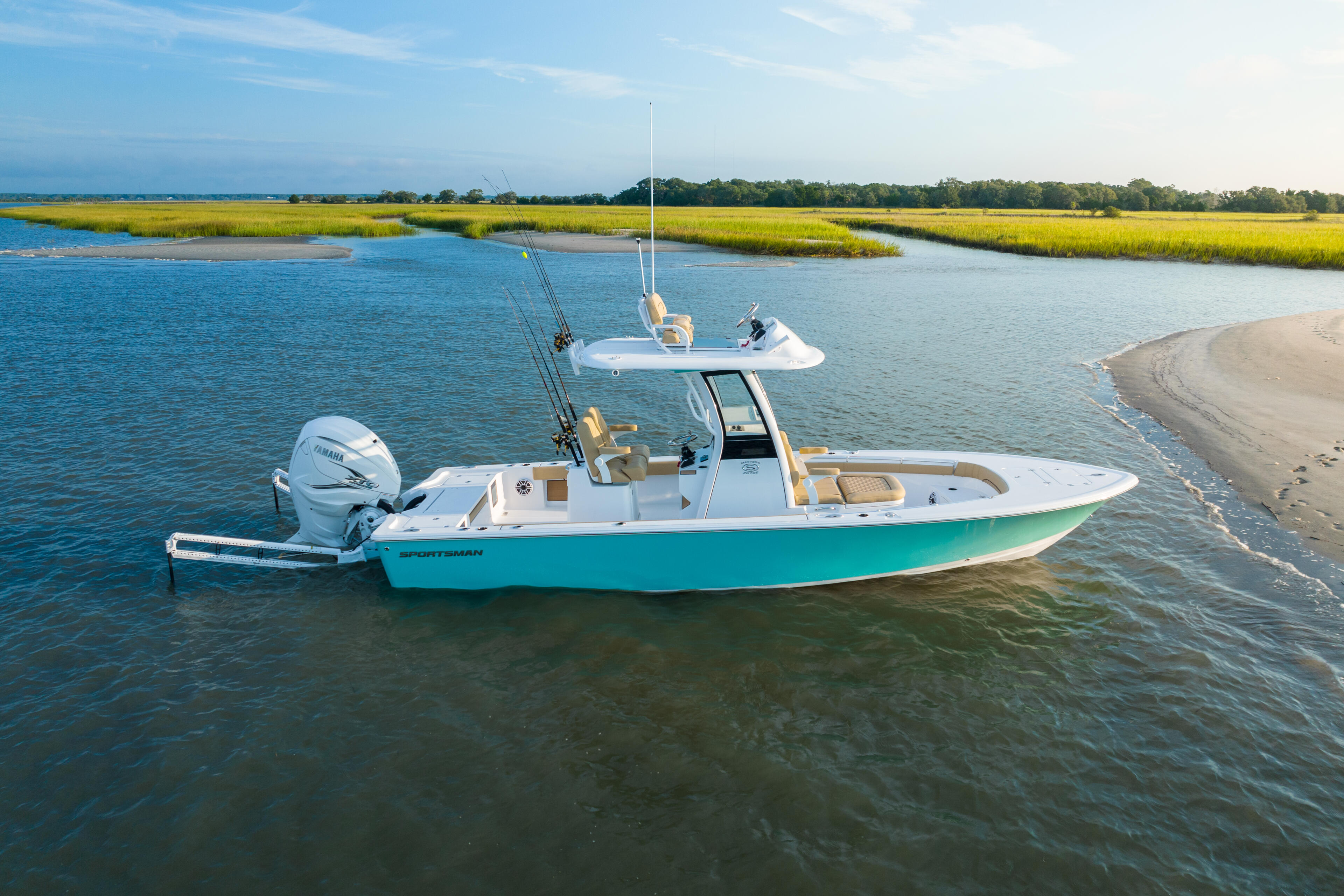 Turquoise and white sportsman boat anchored in shallow marsh waters with sandy beach and grasslands in background