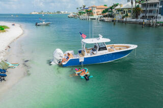 Blue and white center console boat anchored in shallow turquoise water with families swimming and relaxing on a sandy beach