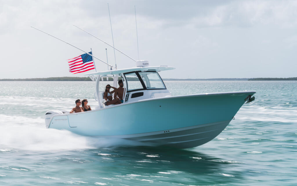Turquoise and white fishing boat with American flag running through shallow turquoise water near a sandbar with passengers aboard