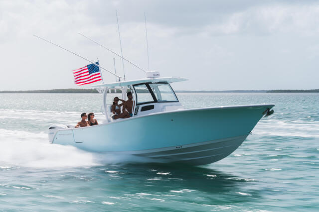 Turquoise and white fishing boat with American flag running through shallow turquoise water near a sandbar with passengers aboard