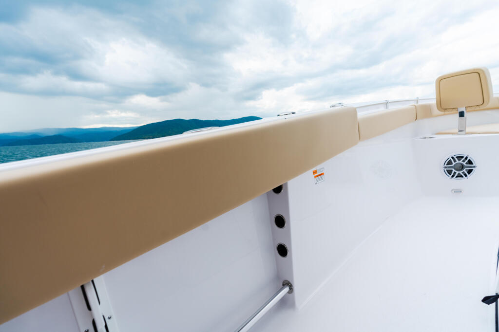 Tan and white boat gunwale with mountains visible across calm blue water under cloudy sky