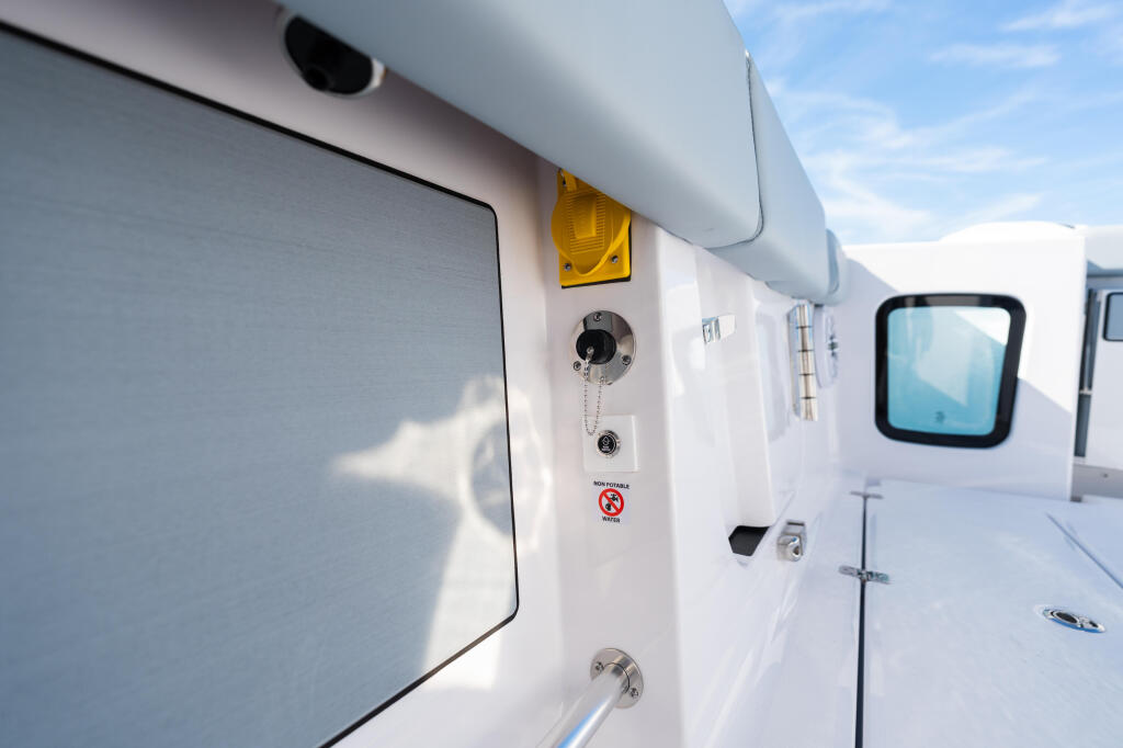 Close-up of boat cabin exterior showing window, yellow light, fuel cap, and safety features against clear sky