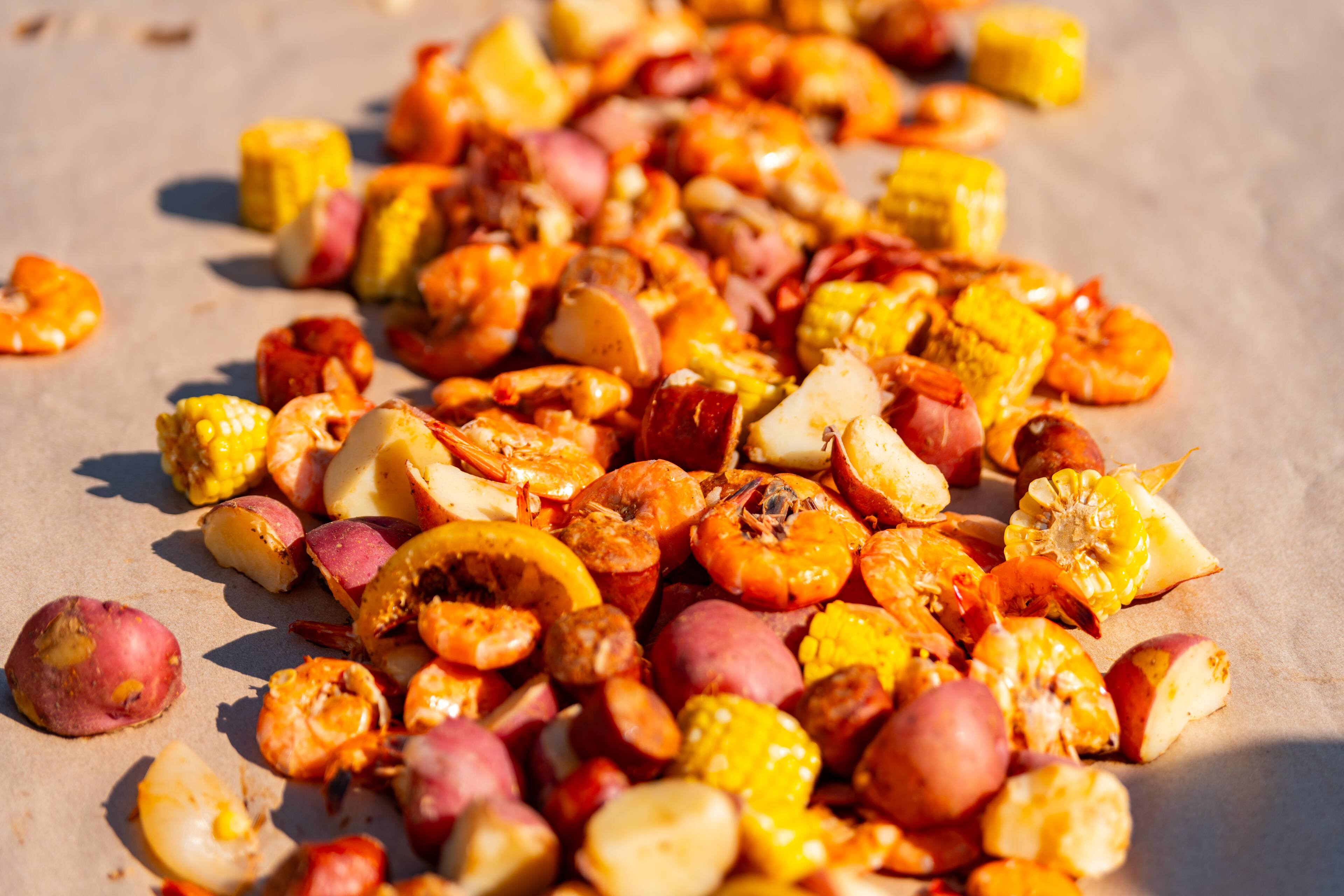 Grilled corn, shrimp, and sausage spread on sand in bright sunlight