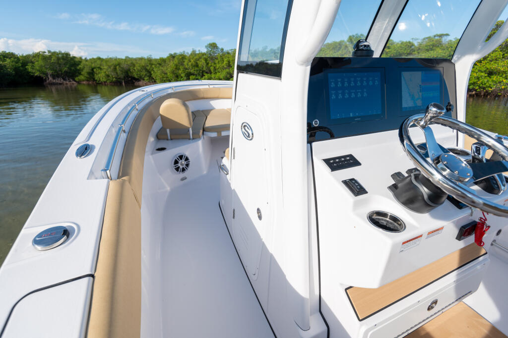 Helm station with dual touchscreen displays, steering wheel, and tan bolster seating overlooking mangrove shoreline