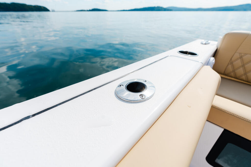 Boat gunwale with tan upholstered seating and chrome hardware overlooking calm lake and distant mountains