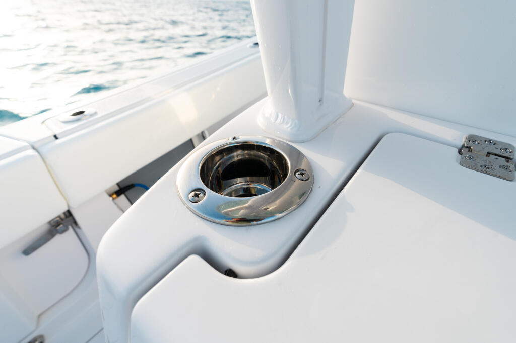 Chrome-rimmed deck fitting with open hatch on white boat gunwale with ocean in background