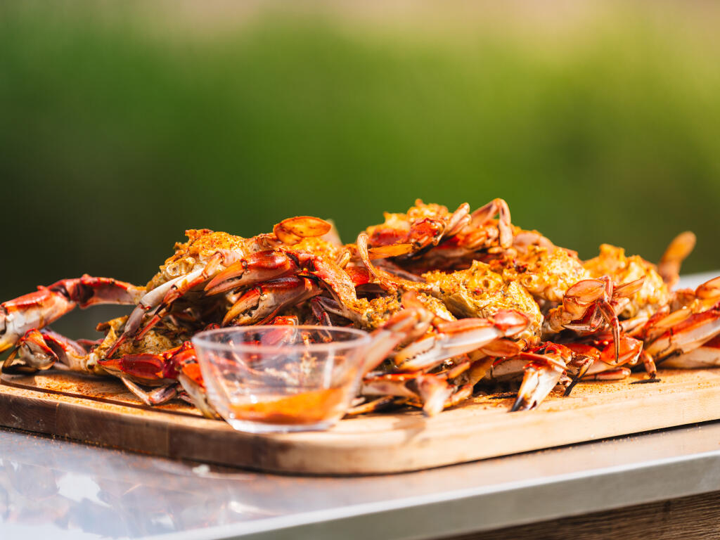 Cooked crabs on a wooden board with melted butter sauce and blurred green background
