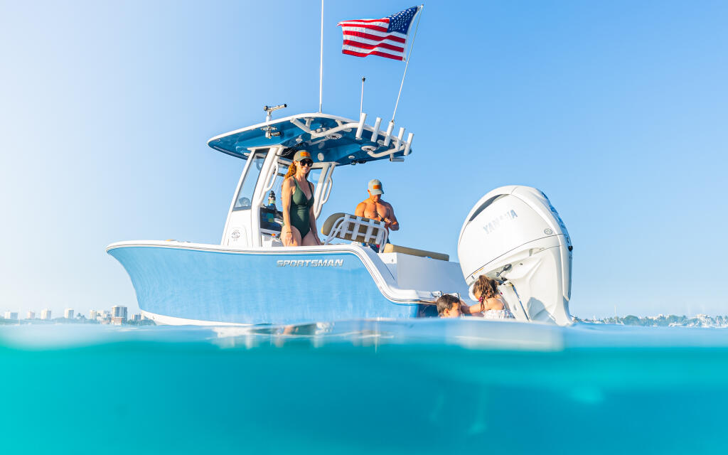 Family swimming and relaxing at a shallow sandbar next to a blue and white center console boat flying an American flag