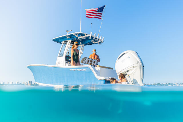 Family swimming and relaxing at a shallow sandbar next to a blue and white center console boat flying an American flag