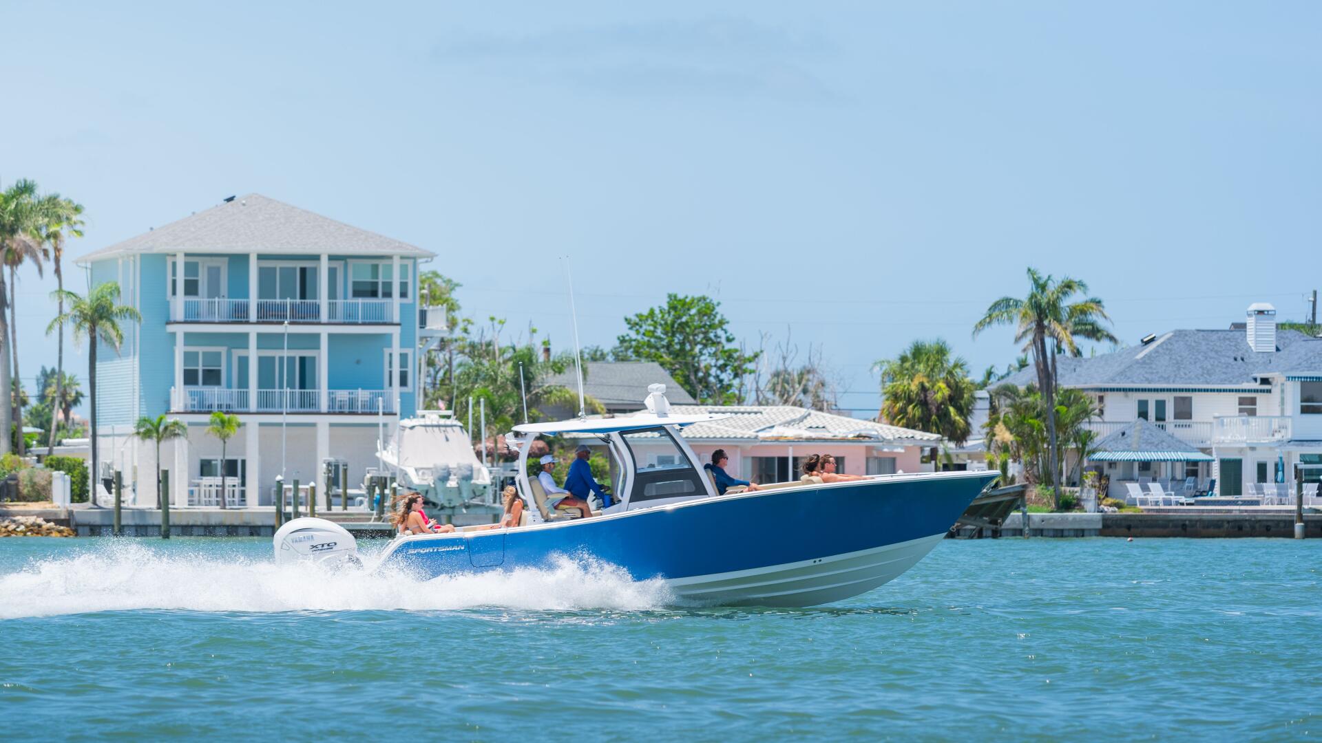 Blue center console boat running at speed past waterfront homes with palm trees