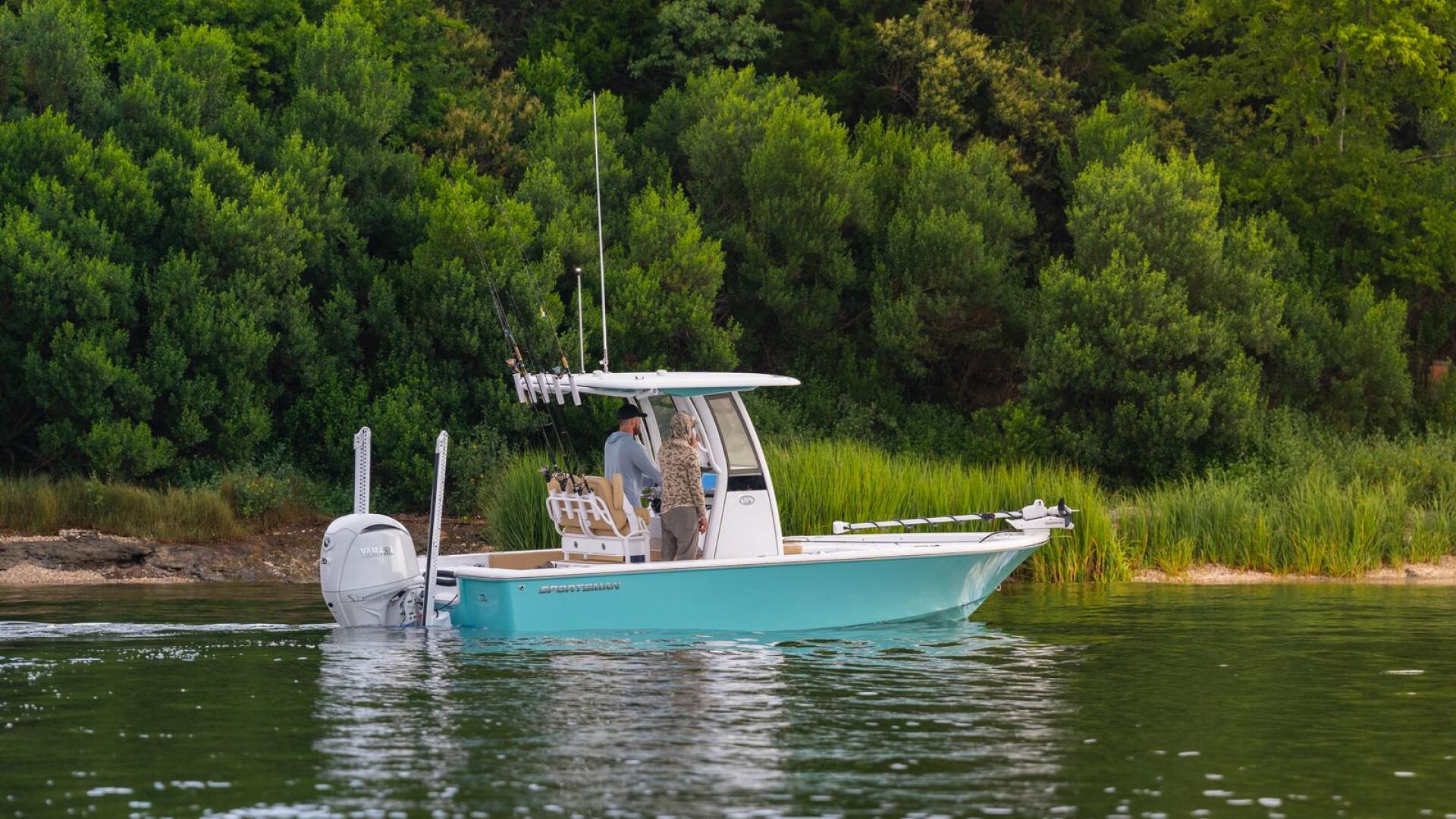 Turquoise and white fishing boat anchored near a forested shoreline with calm green water