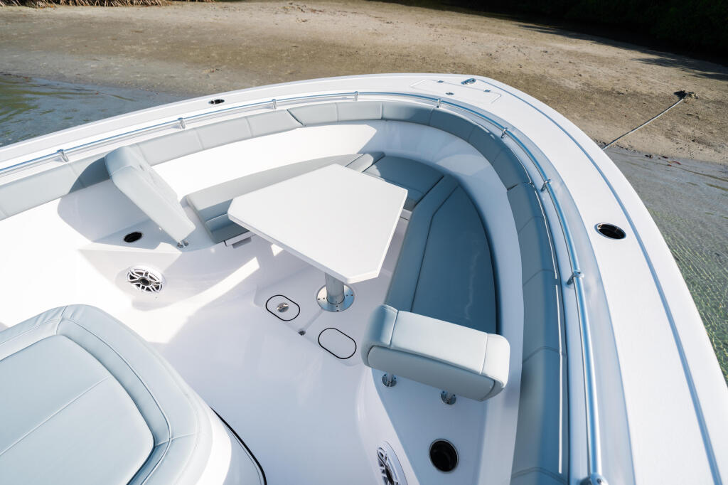 Overhead view of white center console boat with blue seating, helm controls, and storage compartments docked at sandy beach