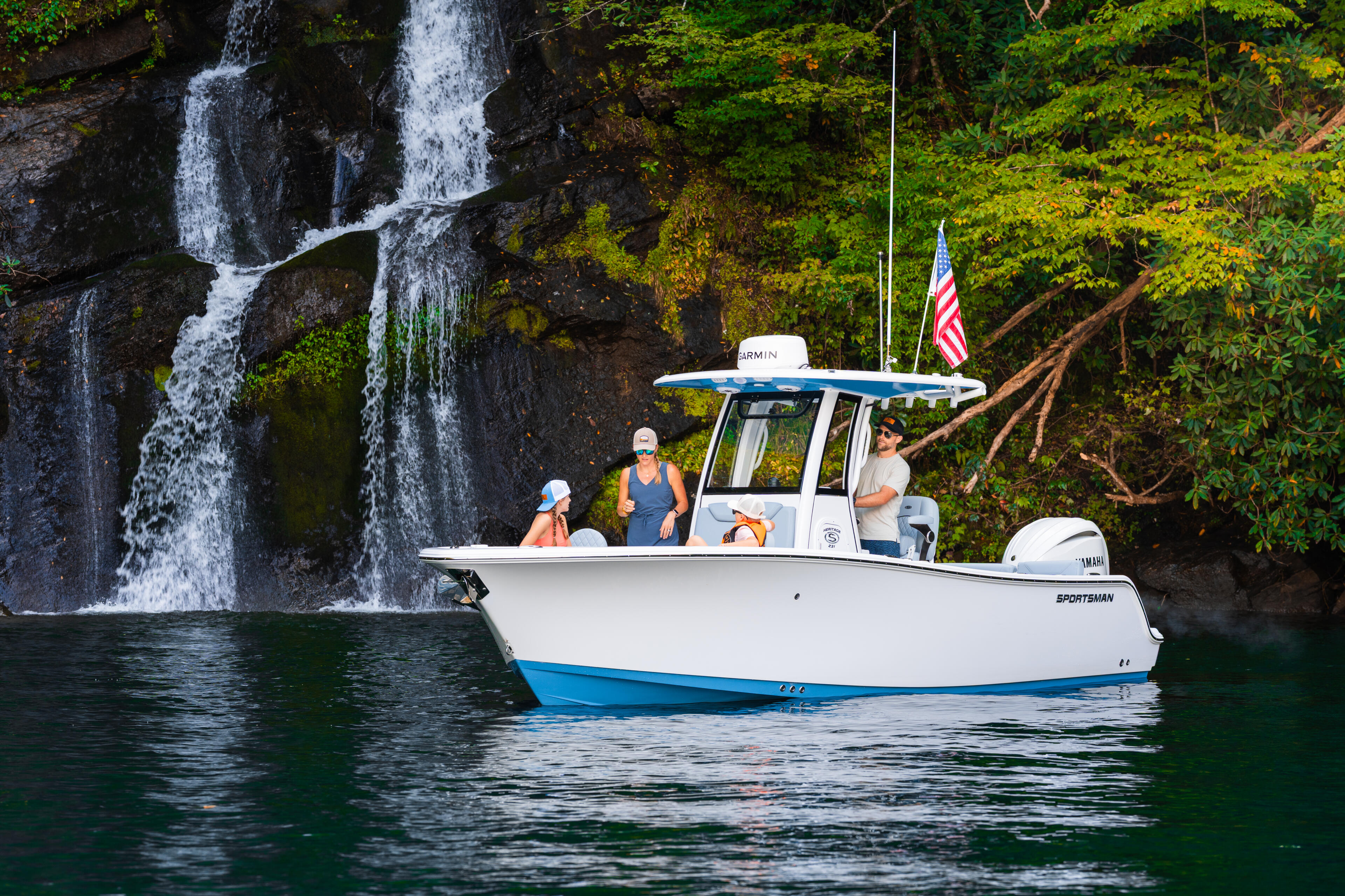 Sportsman boat with three people anchored near a scenic waterfall in a cove surrounded by lush green vegetation