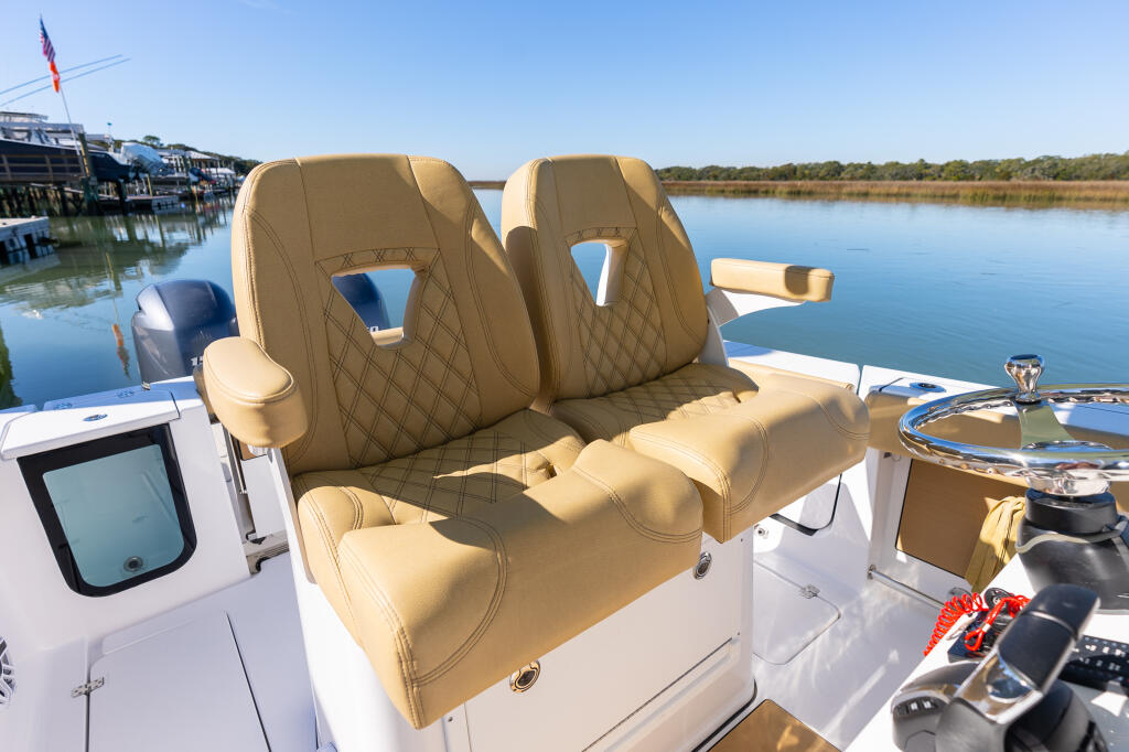 Premium tan quilted captain's chairs at the helm with calm water and marina in background