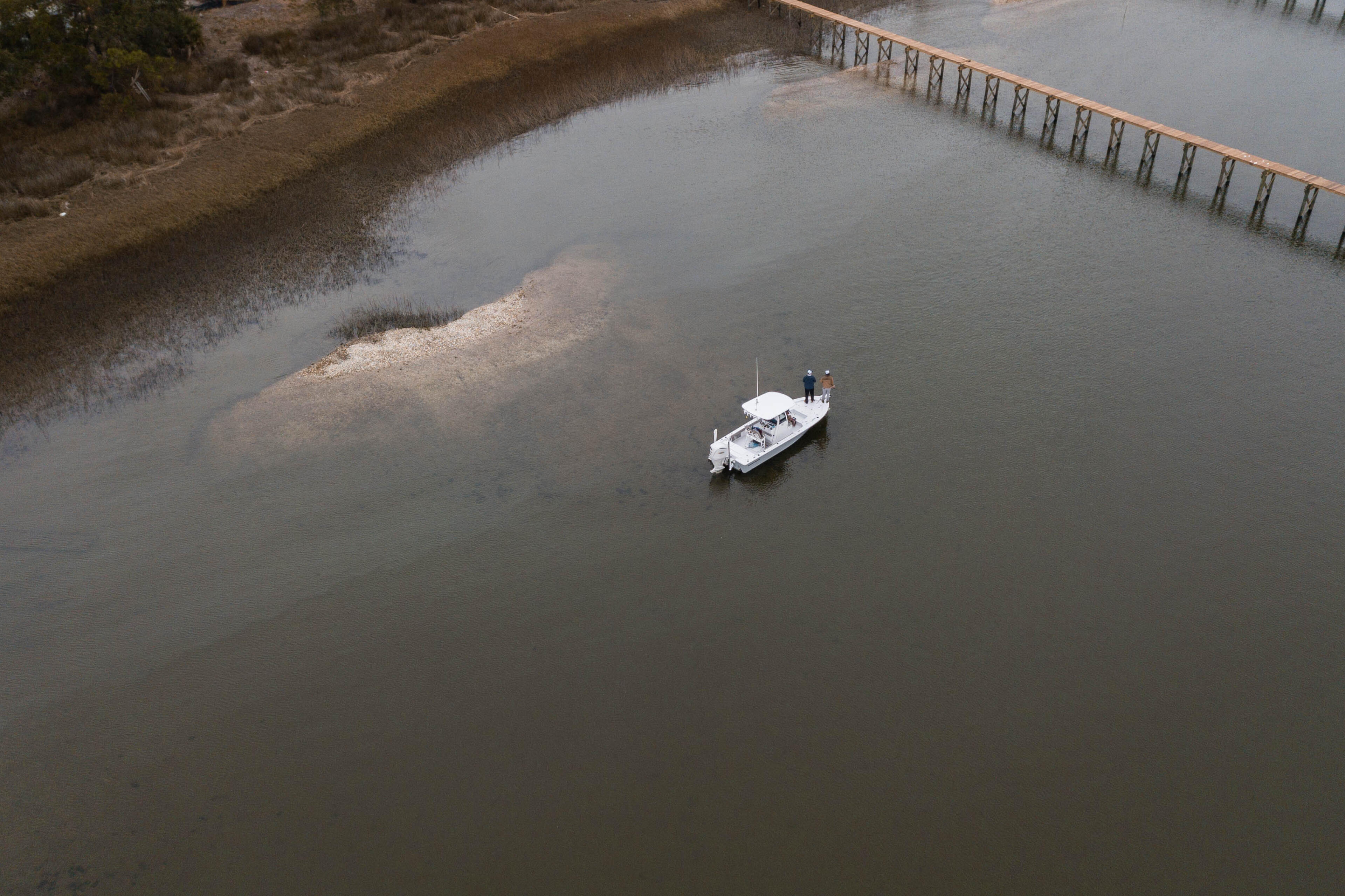 Small white fishing boat anchored in shallow water near a sandbar and wooden pier