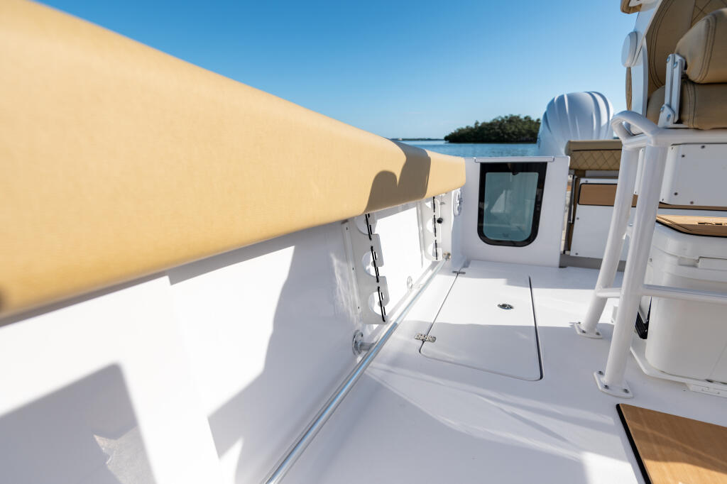 Center console boat's port side deck with retracted tan awning and cabin entry, overlooking calm water and mangroves