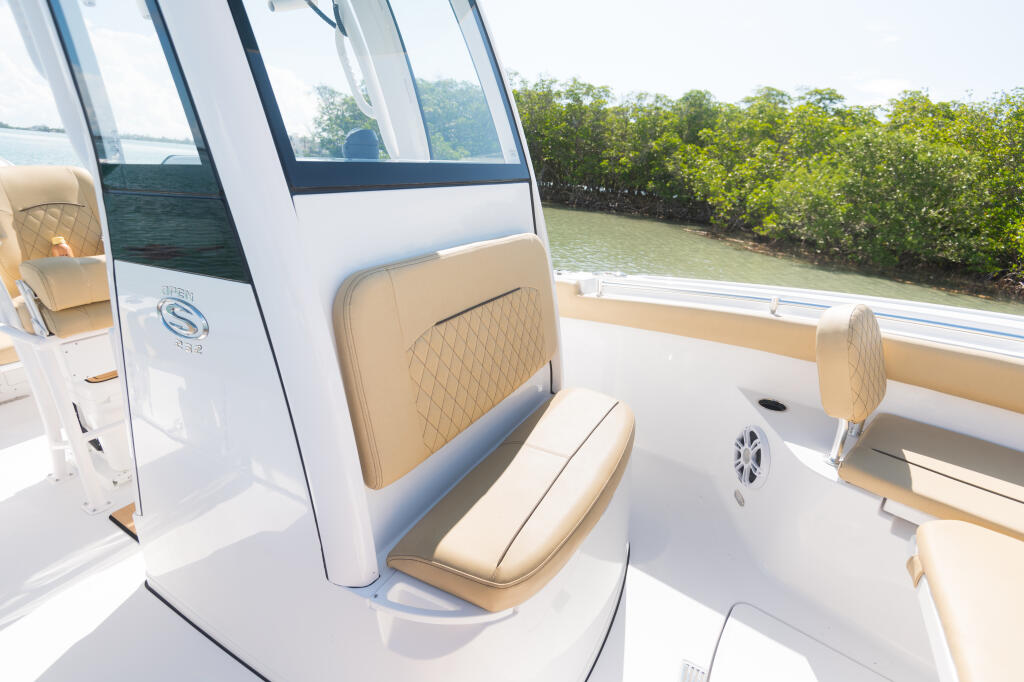 Center console boat cabin interior with quilted tan seating, tinted windows, and hard-top shade overlooking mangroves