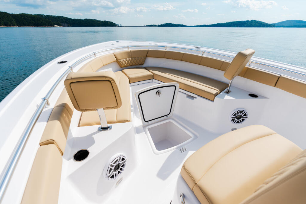 Spacious bow seating area of a white boat with tan cushions overlooking calm blue water and tree-lined shores