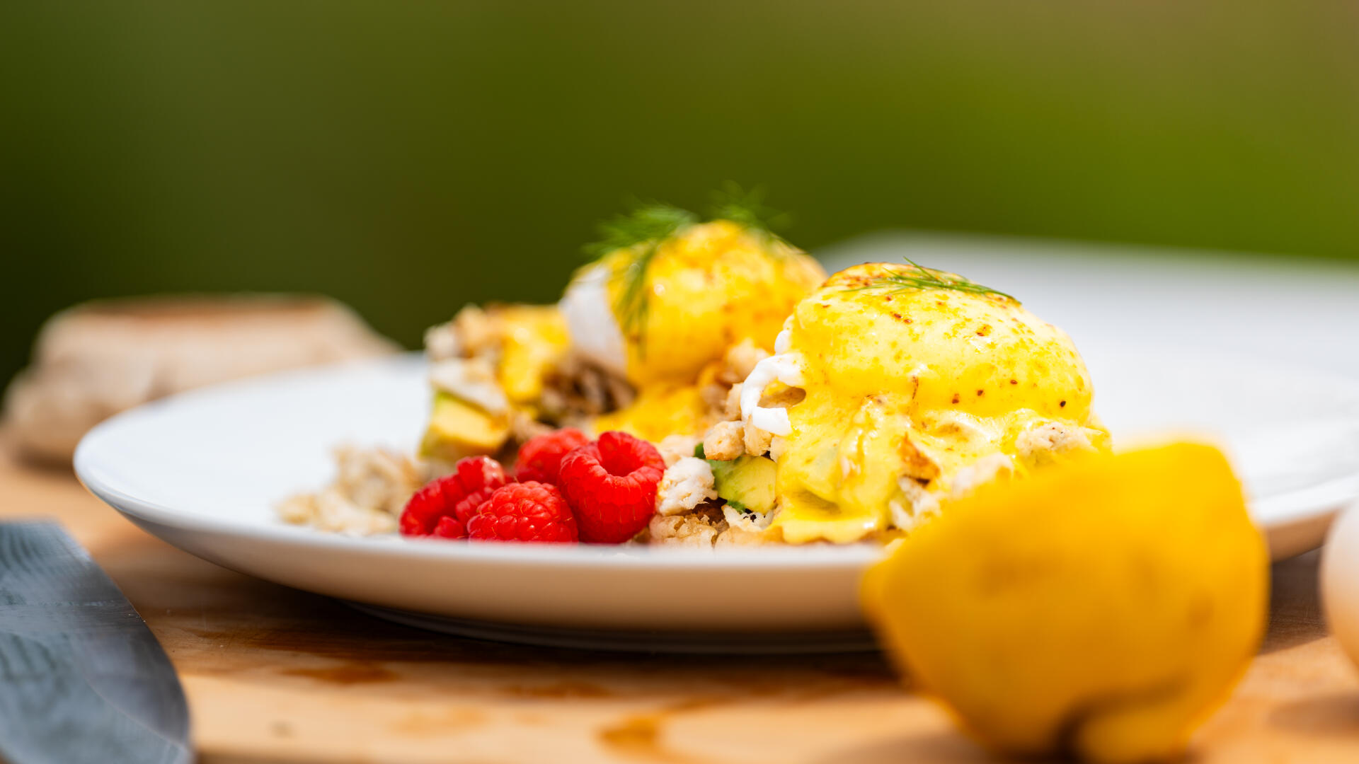 Gourmet crab Benedict with poached eggs, hollandaise, fresh raspberries and lemon garnish on white plate