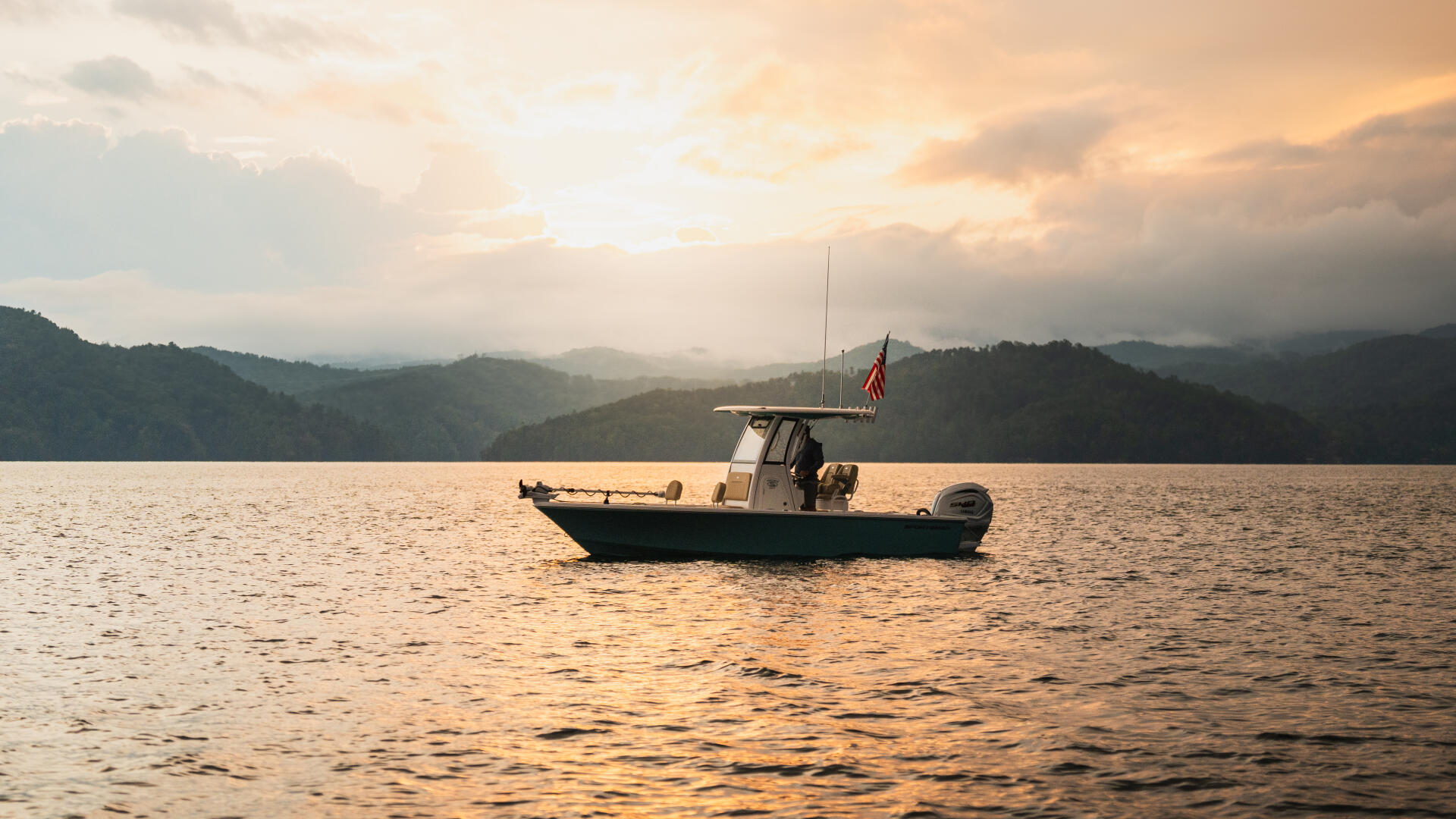 Fishing boat anchored on calm water at golden hour with forested mountains in the background