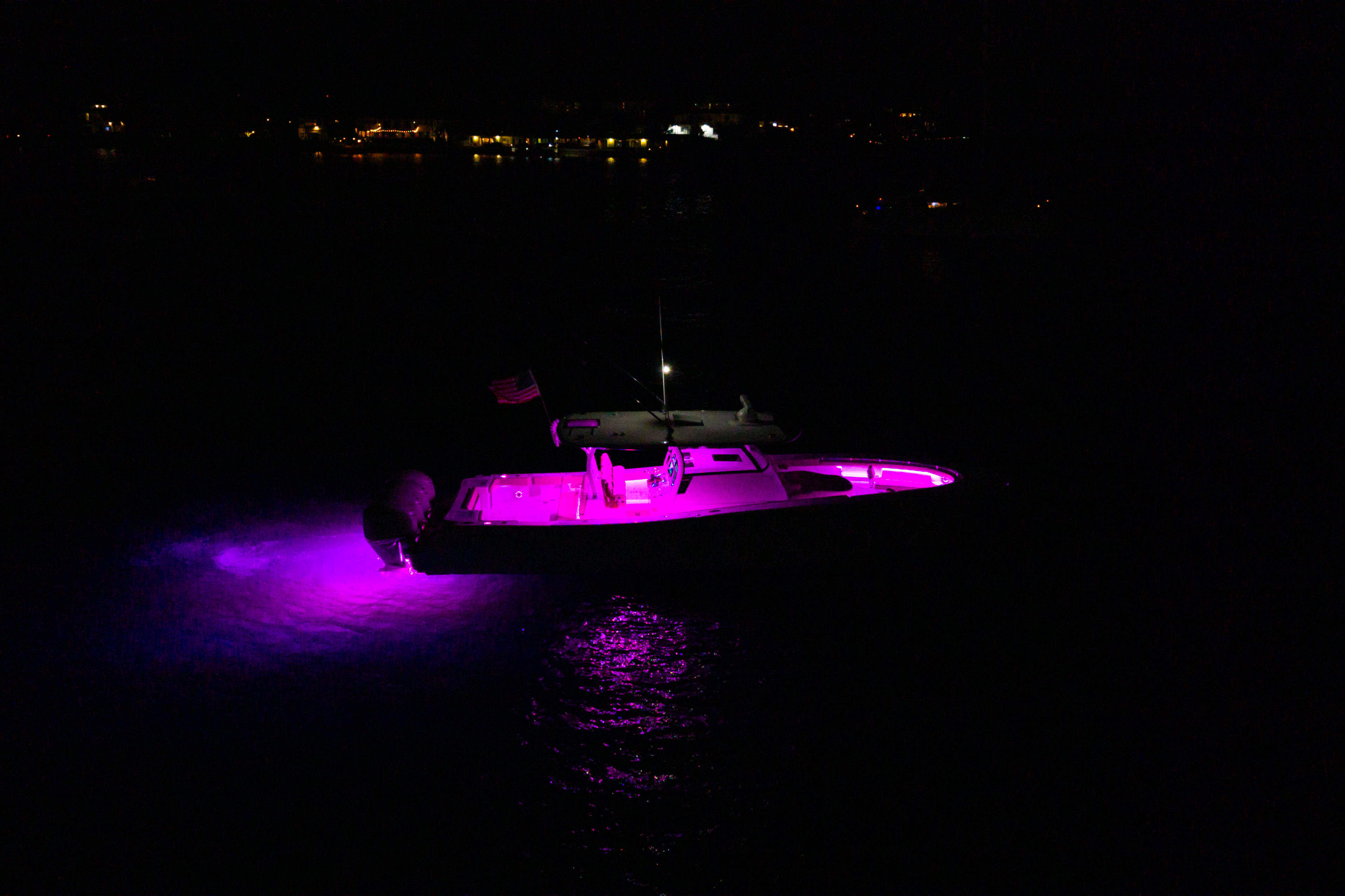 Boat illuminated with vibrant magenta RGB lighting at night on dark water