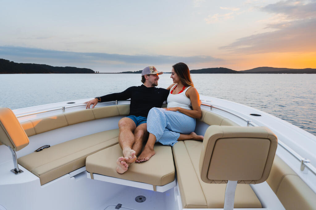 Couple relaxing on the bow seating of a center console boat at sunset on calm water