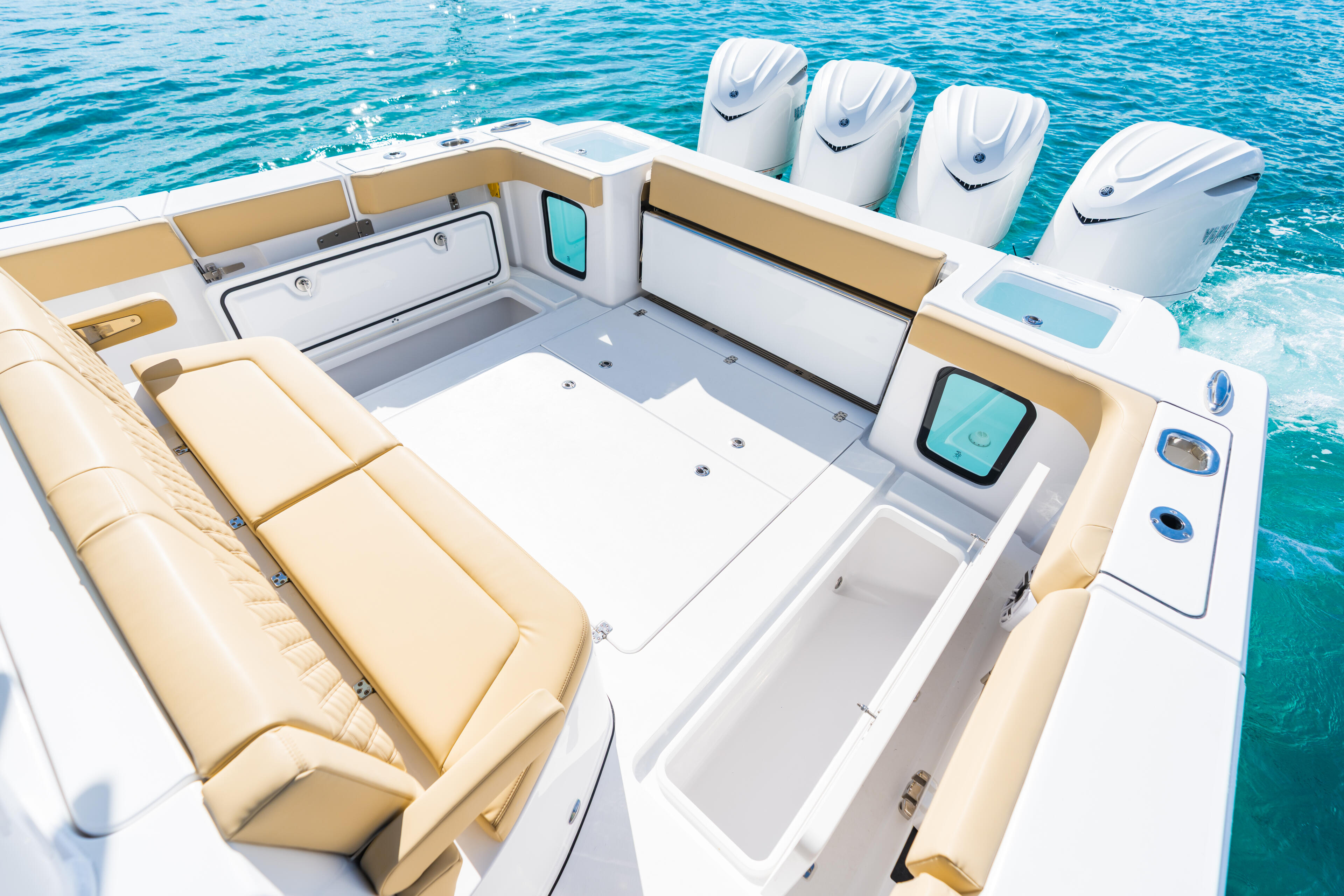 Center console boat cockpit with beige seating, white outboard engines, and open fish storage in calm turquoise water
