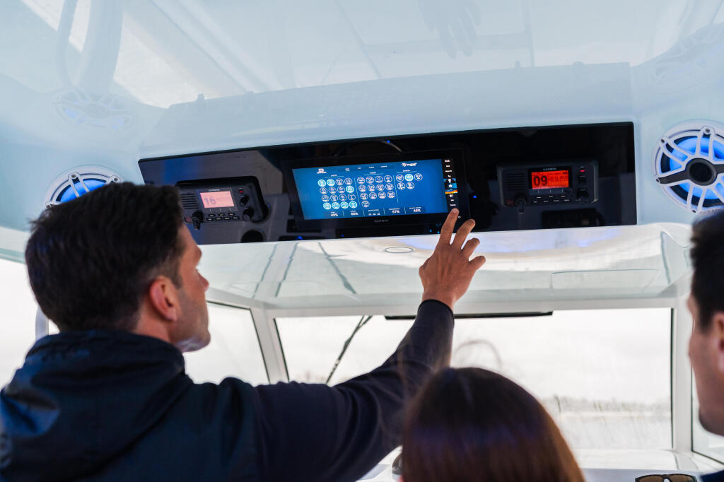 Man operating touchscreen GPS display at helm with couple aboard boat