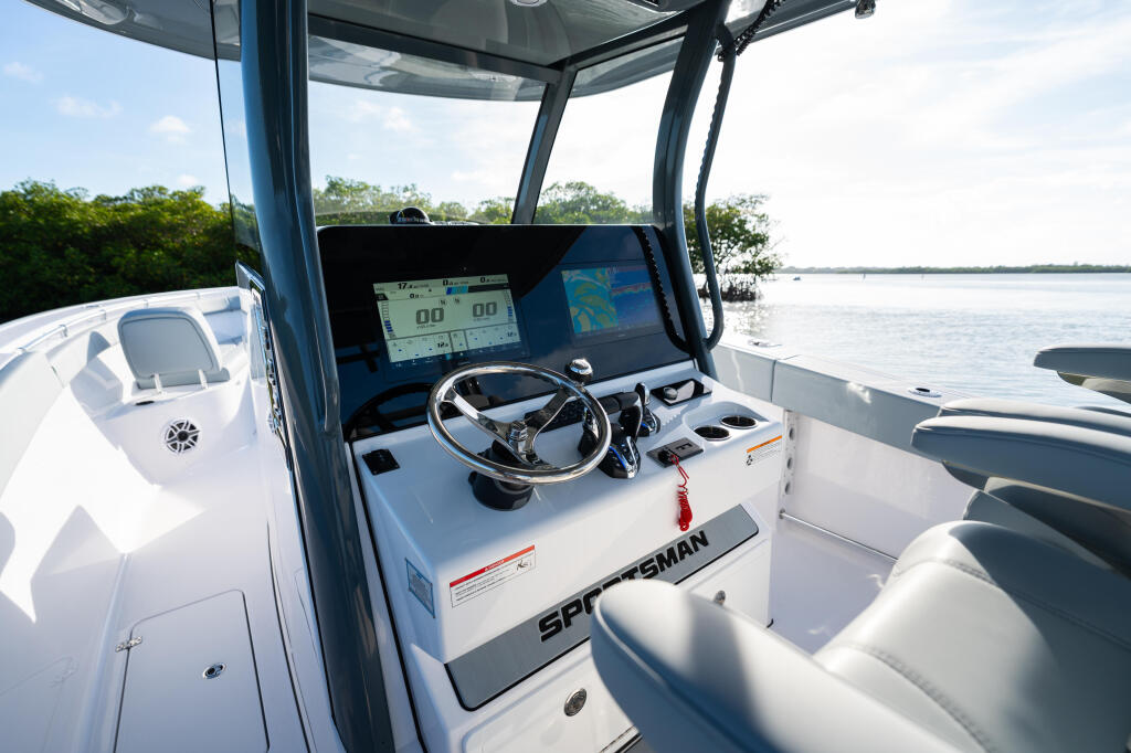 Sportsman center console helm with GPS electronics, steering wheel, and hard-top canopy overlooking calm coastal waters