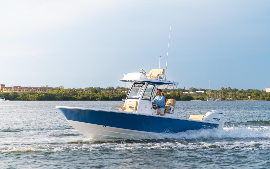 Blue and white center console boat running through shallow coastal waters with man at helm and green shoreline in background