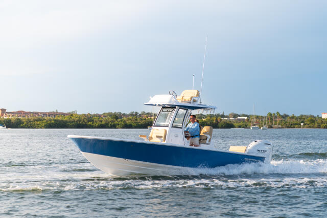Blue and white center console boat running through shallow coastal waters with man at helm and green shoreline in background