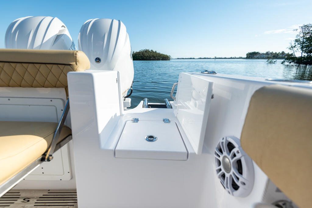 Center console boat interior with tan upholstered seating, white engines, and audio speakers overlooking calm blue water