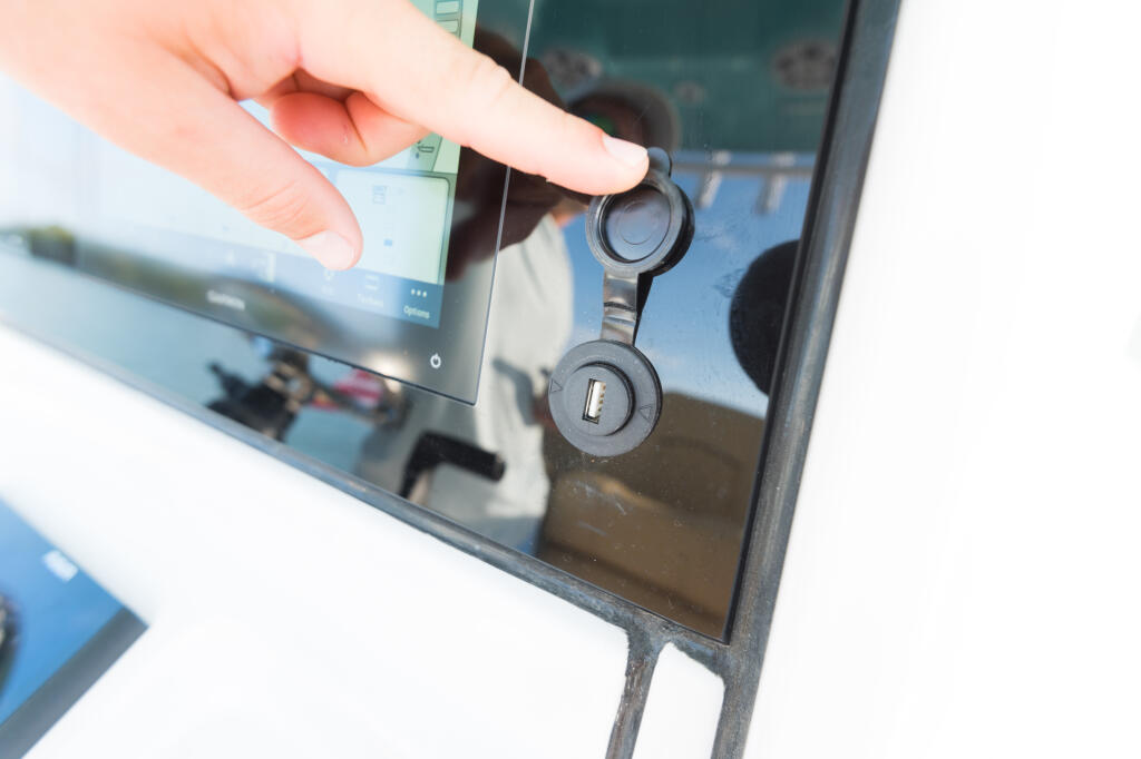 Hand inserting USB plug into dual 12V receptacle mounted on boat dashboard