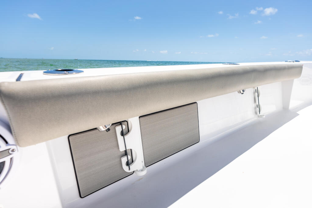Close-up of white gunwale with folding rod racks and storage compartments overlooking shallow turquoise waters