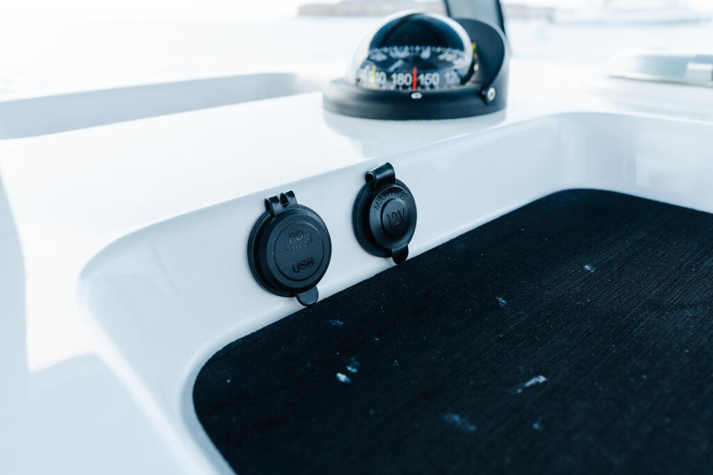 Boat helm console showing compass, navigation electronics, and USB charging ports on white console with black mat below