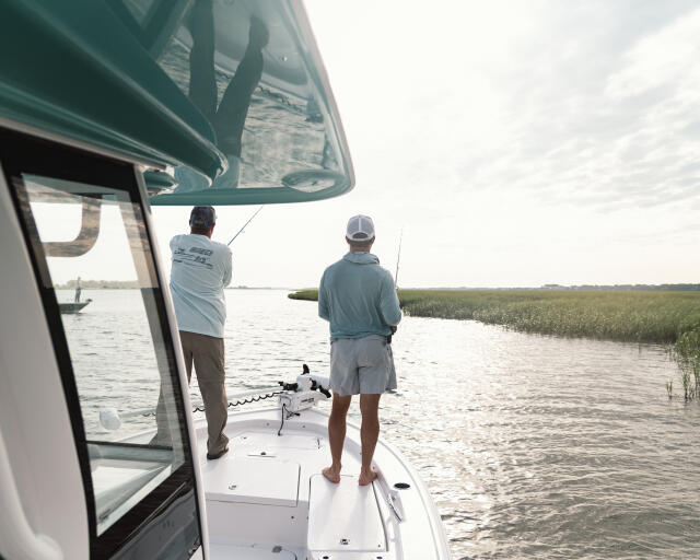 Two anglers fishing from the bow of a center console boat in shallow marsh waters